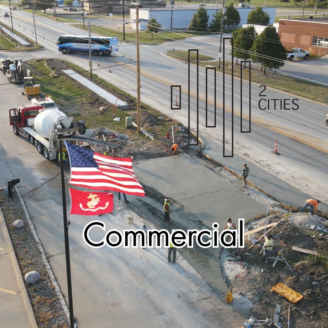 Construction site with workers and equipment on a road, featuring an American flag and a Marine Corps flag.